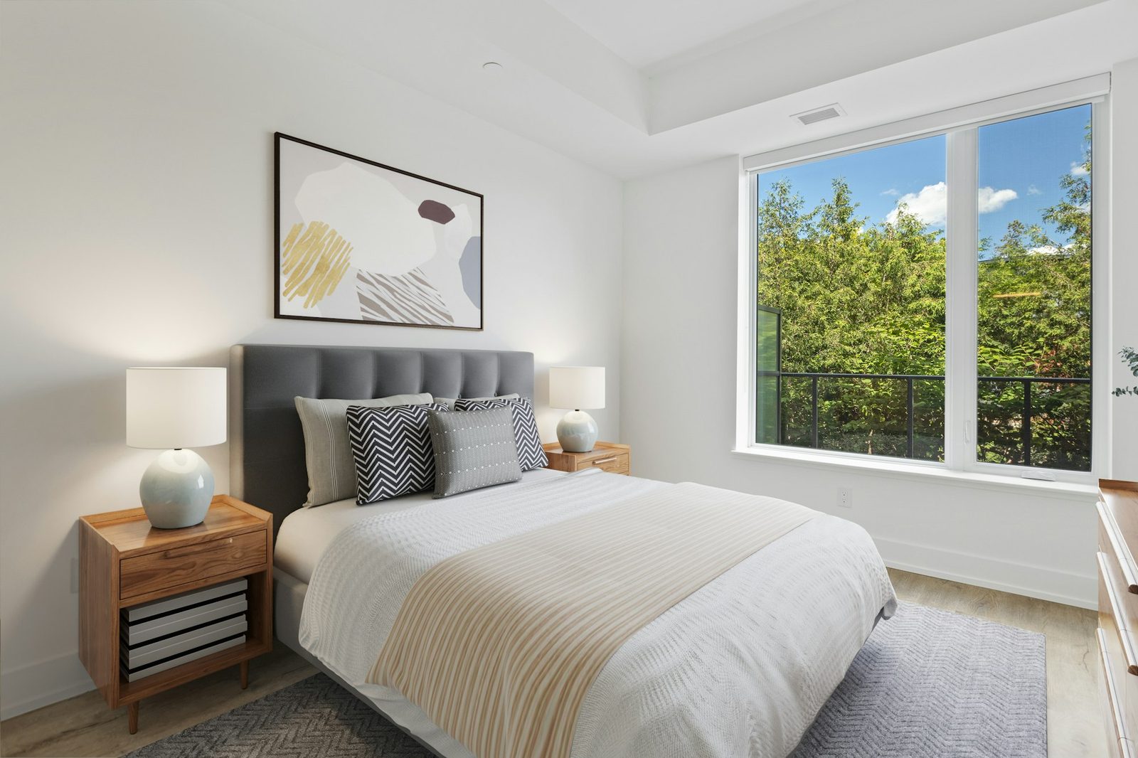 Bedroom with a gray headboard, a queen bed, wooden nightstands and a window onto trees