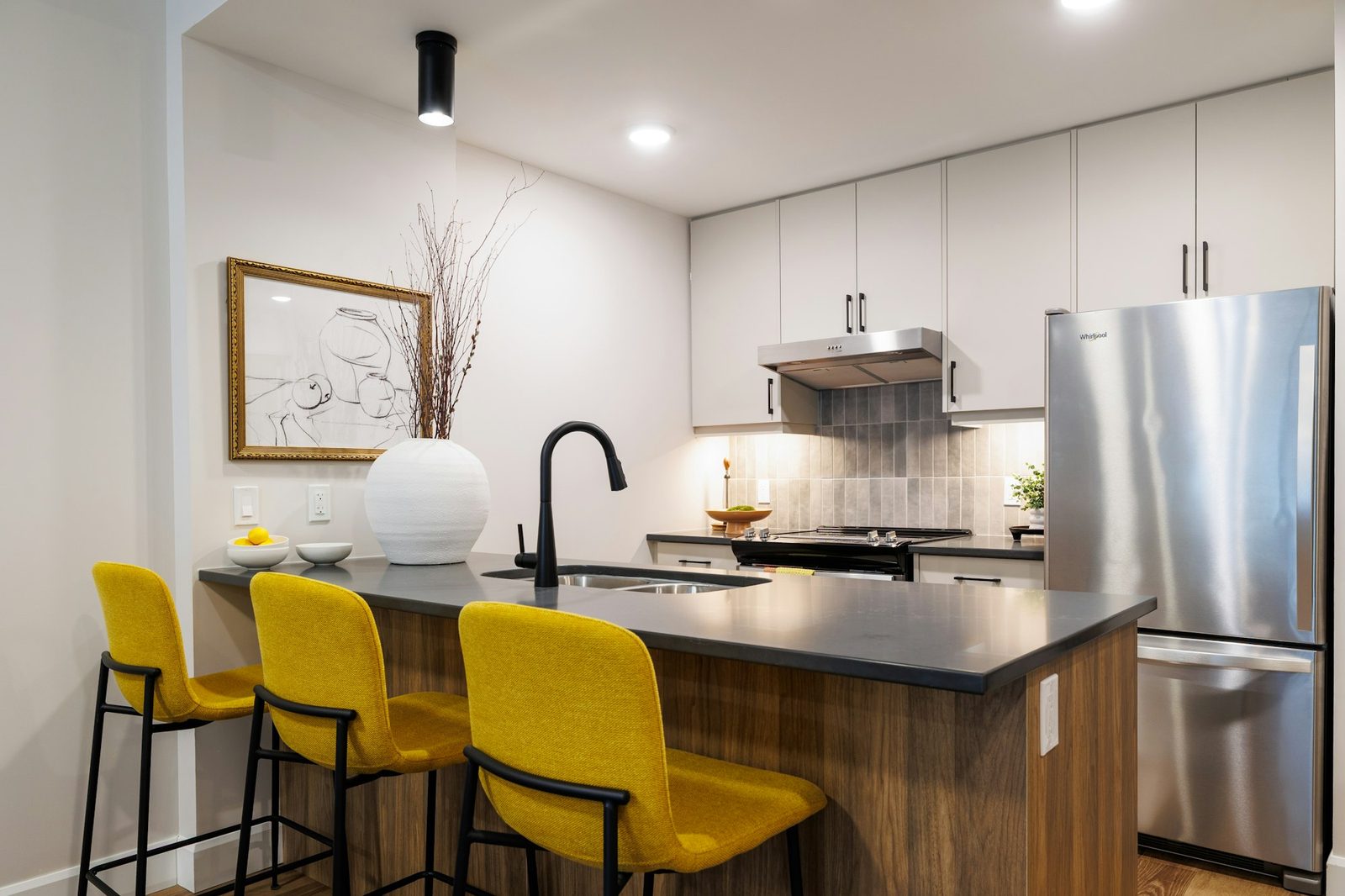 Kitchen with white cabinets, a stainless steel fridge and a breakfast bar with three yellow stools