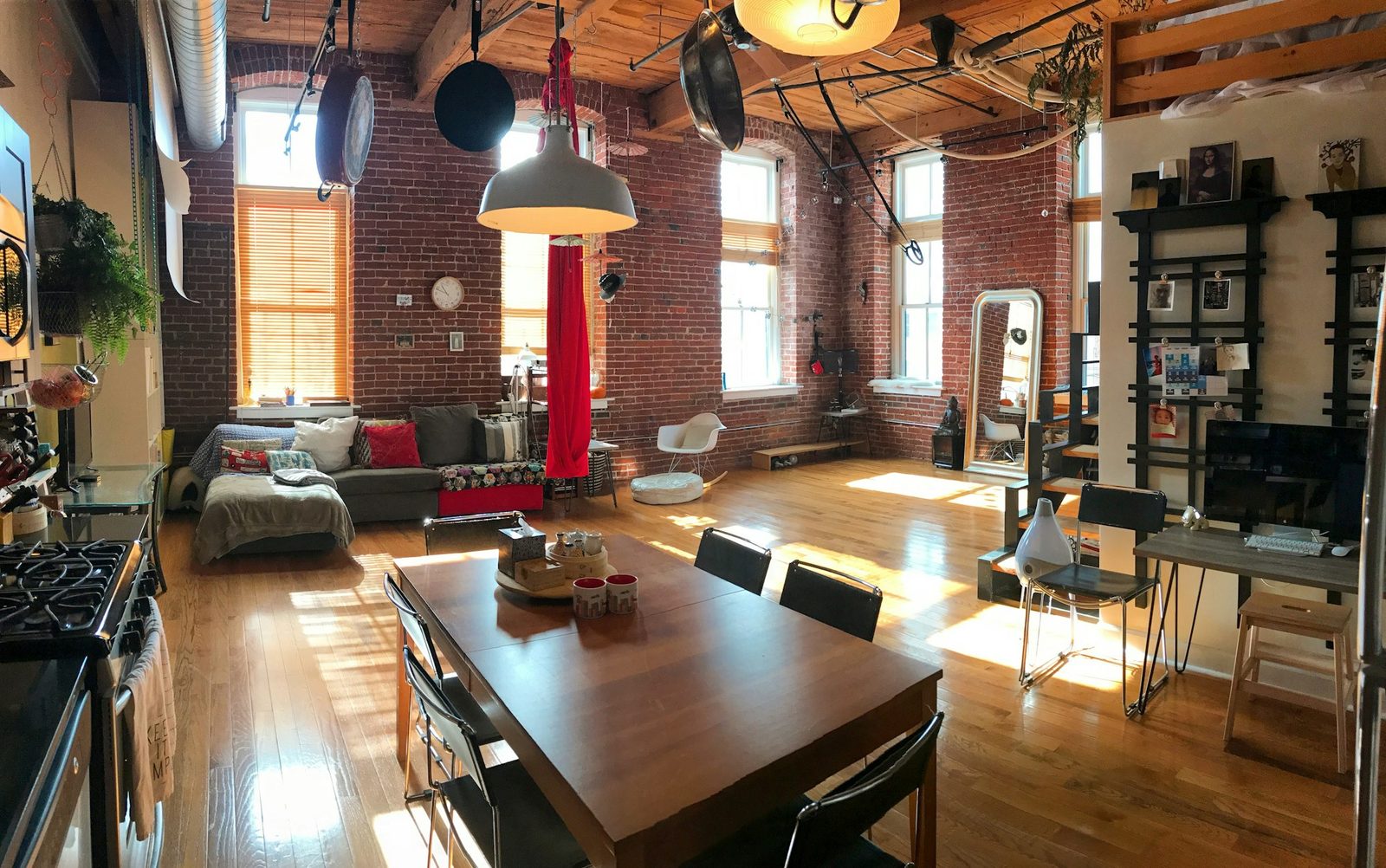 Open room with exposed brick, a dining table, a sofa and tall windows