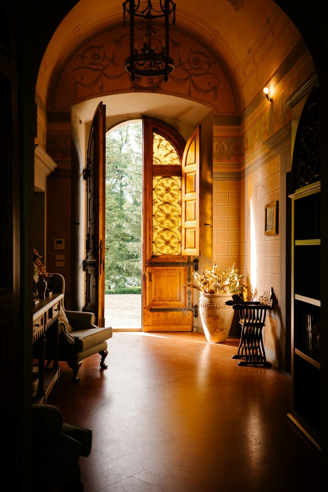 An arched entrance with an open timber door, a lantern overhead and a view of trees outside