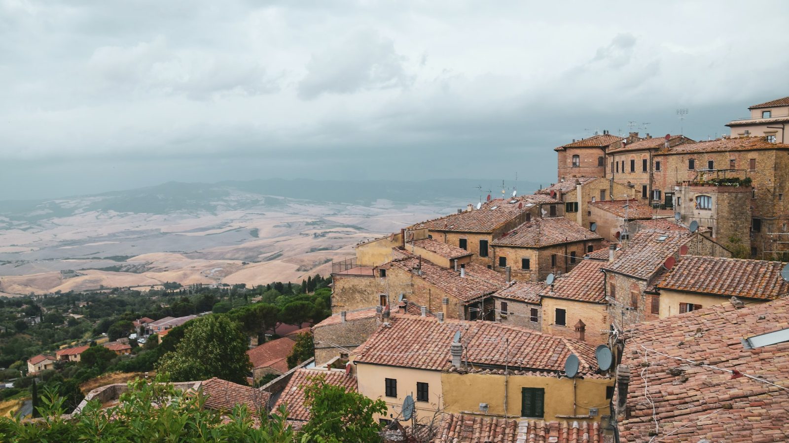 Terracotta roofs of a hill town under a cloudy sky, with hills beyond