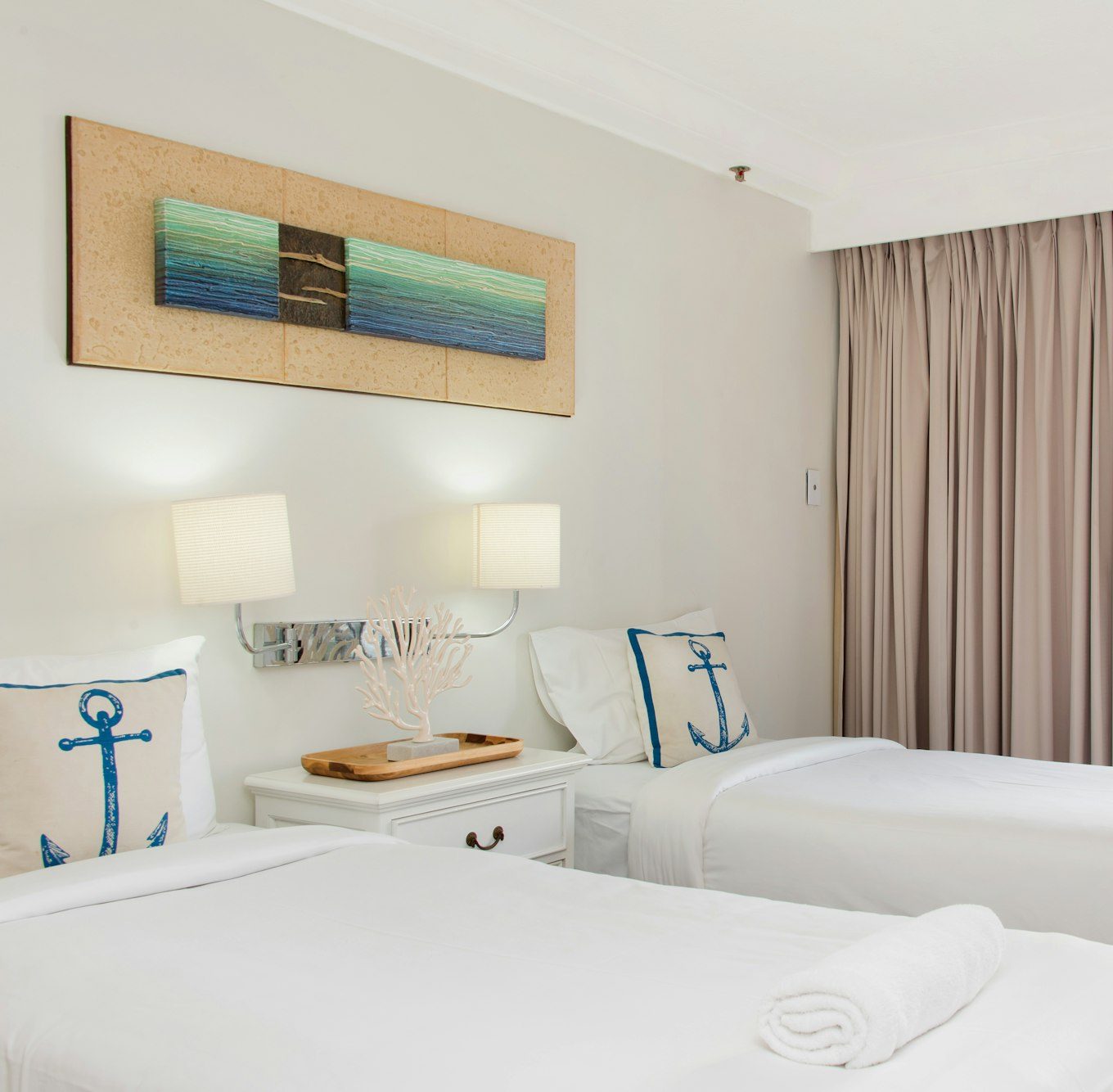 Two single beds with white linen and anchor cushions, a pale painting above them and a balcony door.