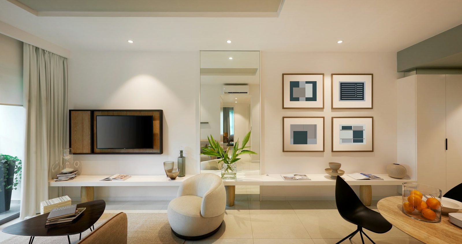 A living area with a wall-mounted TV, framed prints, a white armchair and a long white shelf